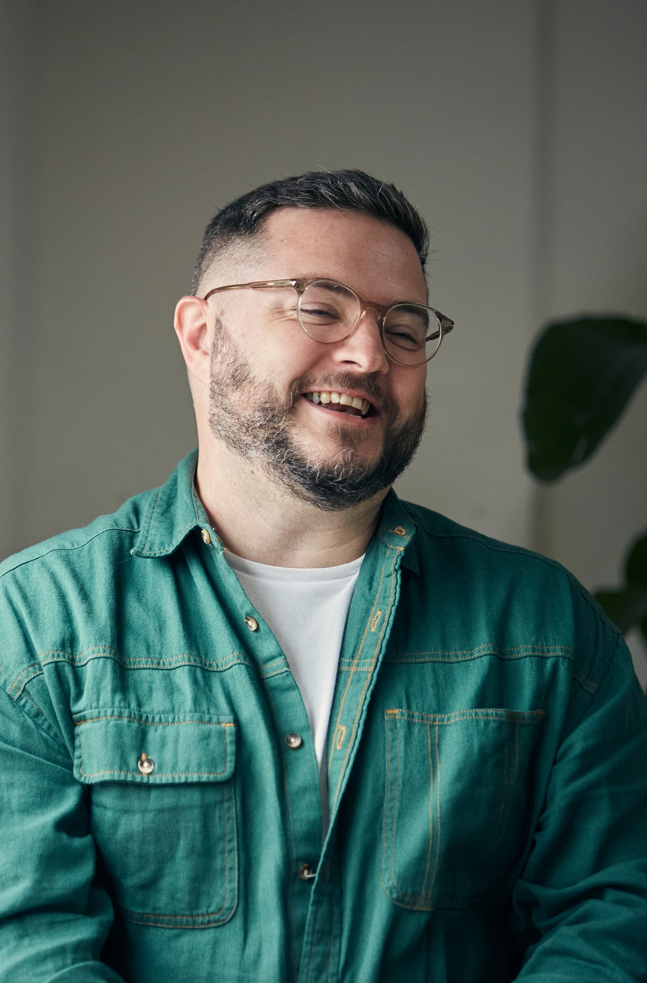 Col is photographed laughing whilst wearing a green shirt and glasses inside the Few and Far offices