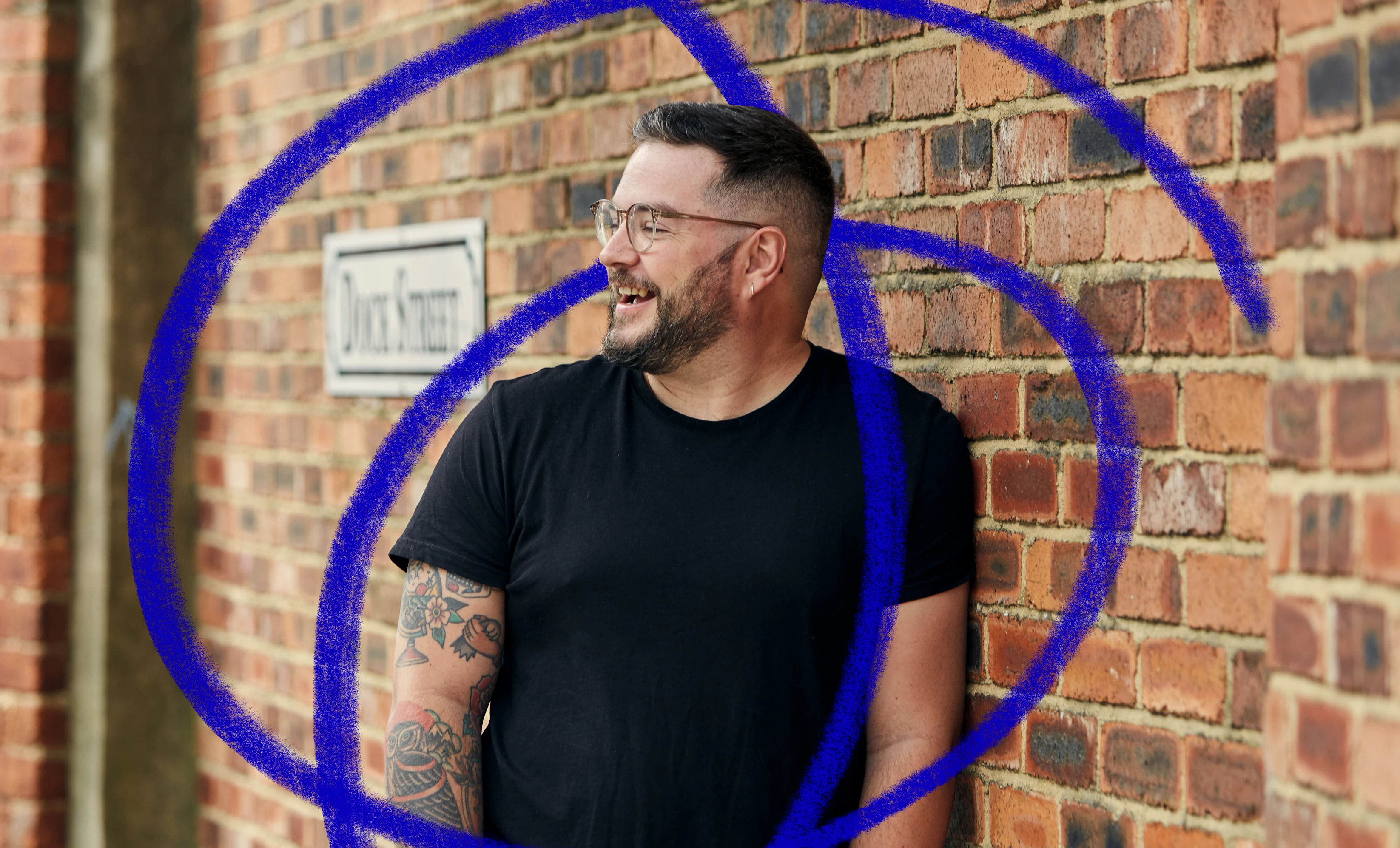 Col is leaning against a red brick wall on Dock Street Leeds, shown are the Mind brand squiggles superimposed around him