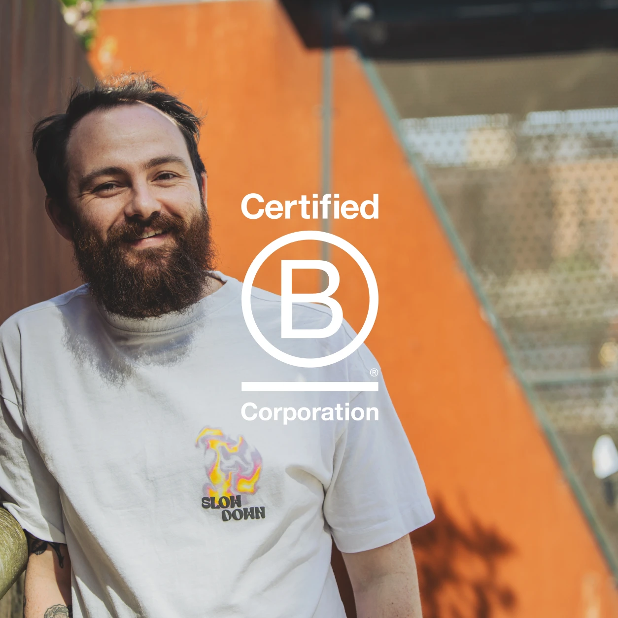 Thomas leans against a fence and smiles for the camera, the B Corp logo is overlaid